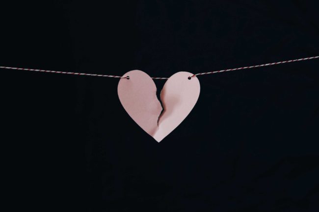 a slightly torn paper heart suspended on a washing line
